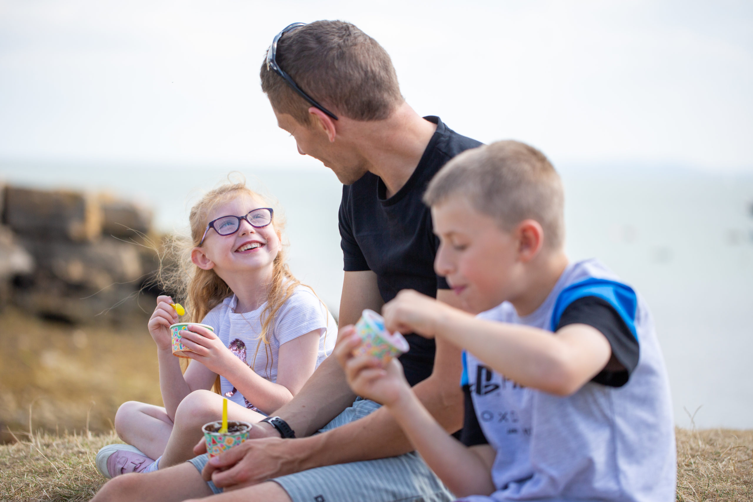 One man and two children eating ice-cream by the sea